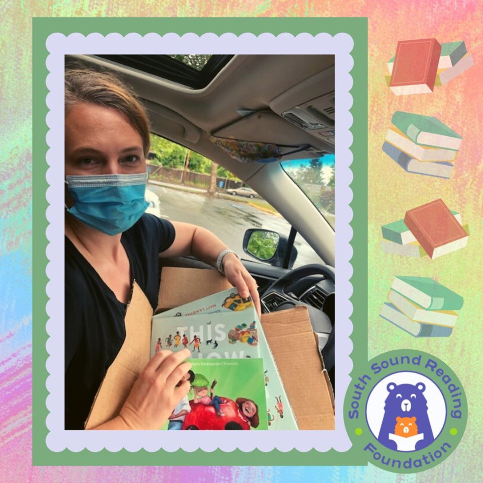 White woman in blue face mask holding box of books in car